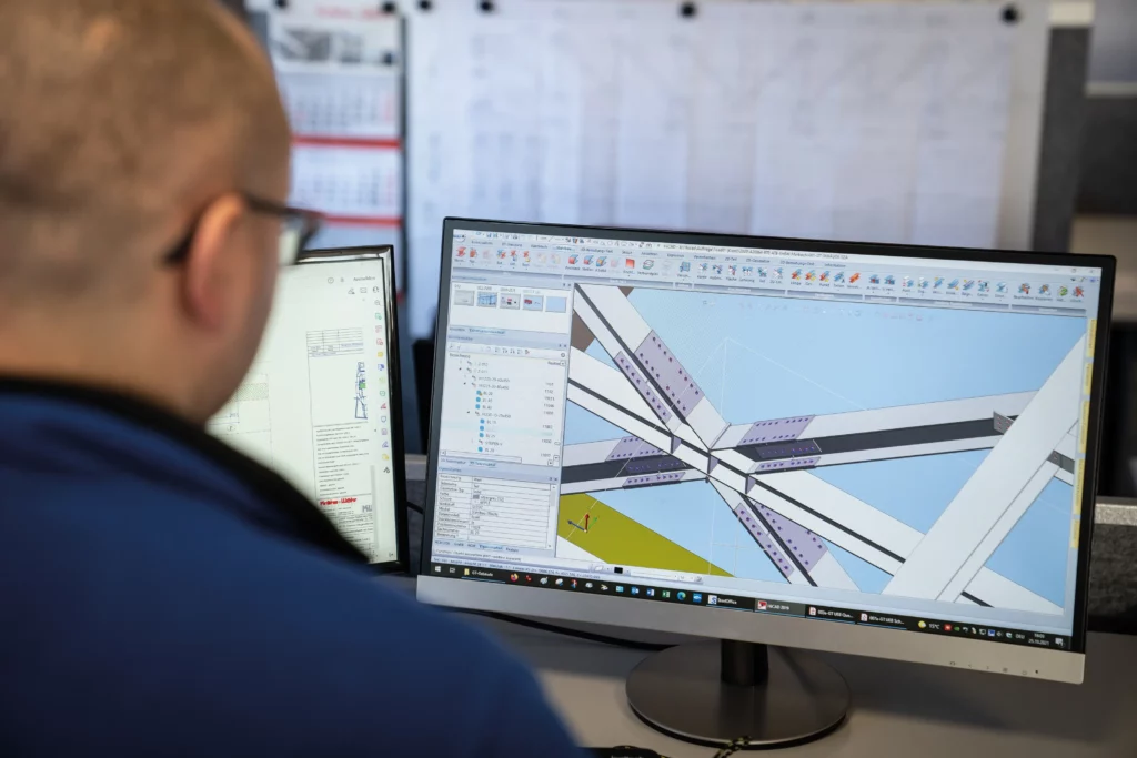 Ein Konstrukteur sitzt vor dem Bildschirm an einer CAD-Software und arbeitet am 3D-Modell einer Stahlkonstruktion